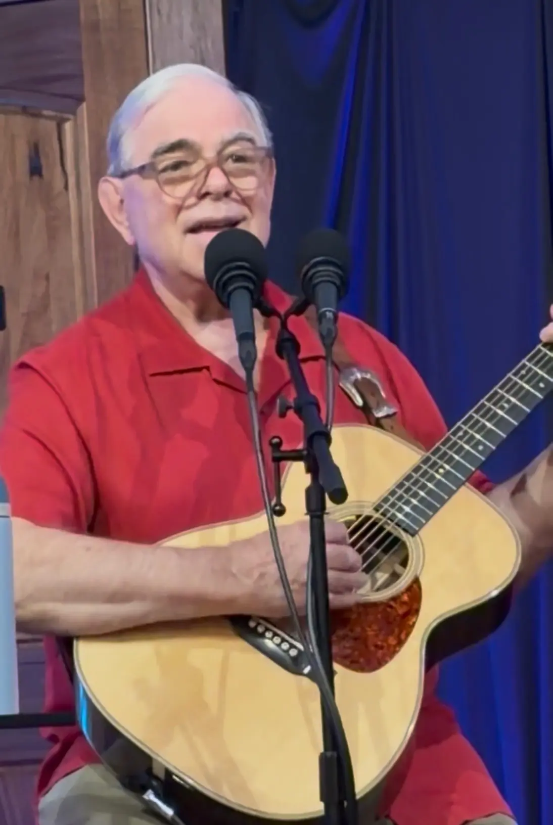 Dave Miller at microphone in red shirt, blue stage curtain