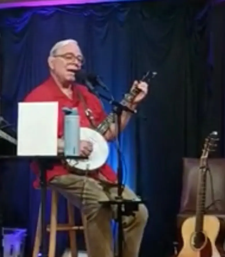 Dave Miller playing banjo on stage in red shirt